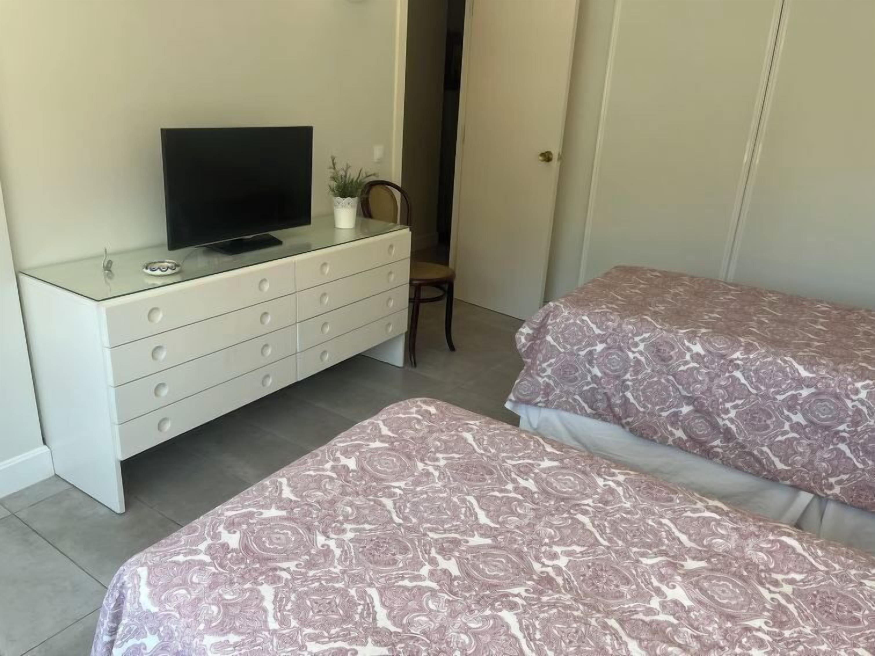 A bedroom with a TV on a dresser, two beds with patterned bedding, a chair, and a door.