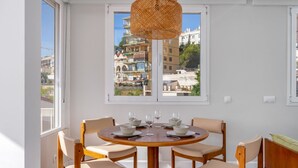 Un coin repas avec une table ronde en bois, quatre chaises et un luminaire suspendu en fibres tressées.