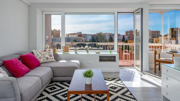 Un salon moderne avec un canapé gris, une table basse et une vue sur la ville grâce à de grandes fenêtres.