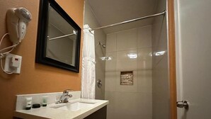 A bathroom with a sink, mirror, hairdryer, and shower.