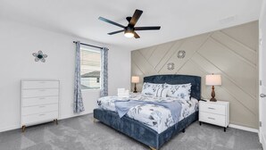 Ein Schlafzimmer mit einem Bett, Nachttischen, einer Kommode, einem Deckenventilator und einem Fenster mit Vorhängen.