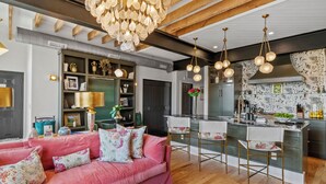 A modern living room with a pink sofa, a wooden ceiling, and a kitchen area with a patterned backsplash. - Top of the Town | Luxury 2BR Adults-Only · Downtown Burnsville · Walk Everywhere (Burnsville)