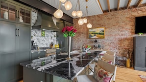 A modern kitchen with a marble island, stainless steel appliances, and a brick wall. - Top of the Town | Luxury 2BR Adults-Only · Downtown Burnsville · Walk Everywhere (Burnsville)