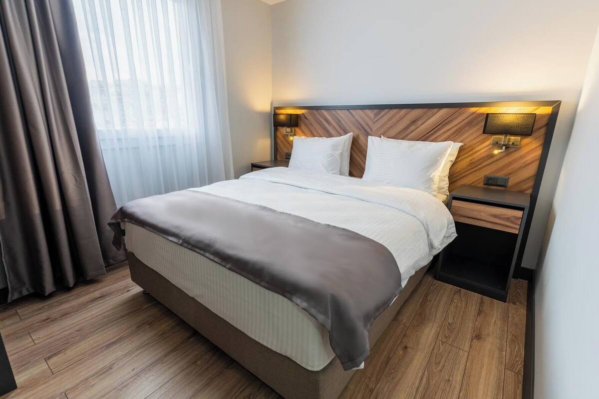 Ett hotellrum med en stor säng, ett träbeklätt sänggavel, två sängbord och ett litet bord.
