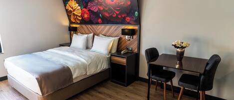 Habitación de hotel con cama, mesita de noche, lámpara y un pequeño comedor con mesa y sillas.