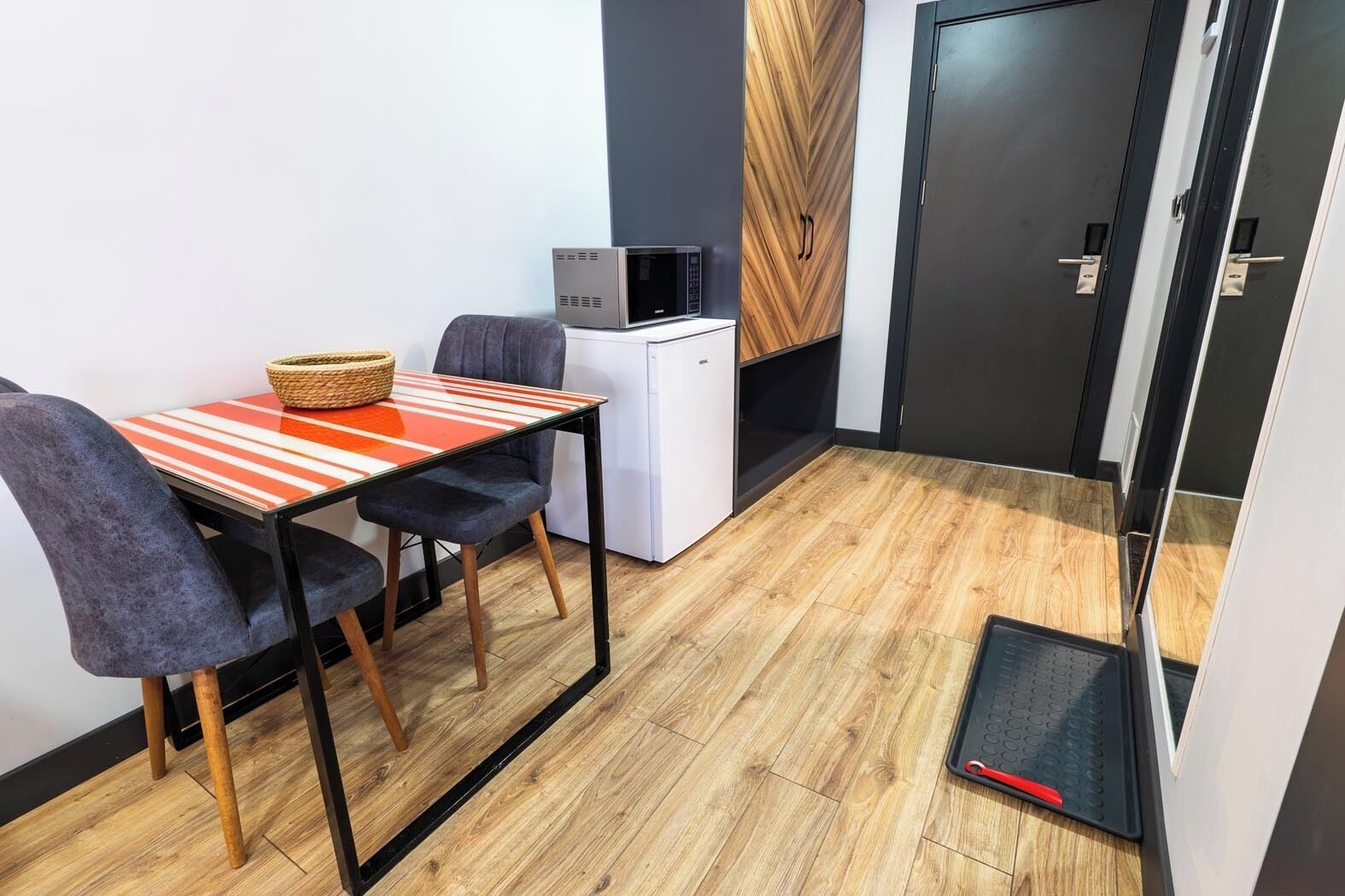 Habitación compacta con una pequeña mesa y dos sillas, un mini refrigerador blanco, un microondas y un armario de madera.