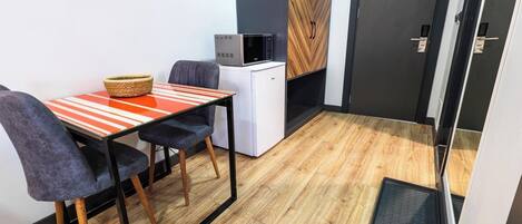 Habitación compacta con una pequeña mesa y dos sillas, un mini refrigerador blanco, un microondas y un armario de madera.