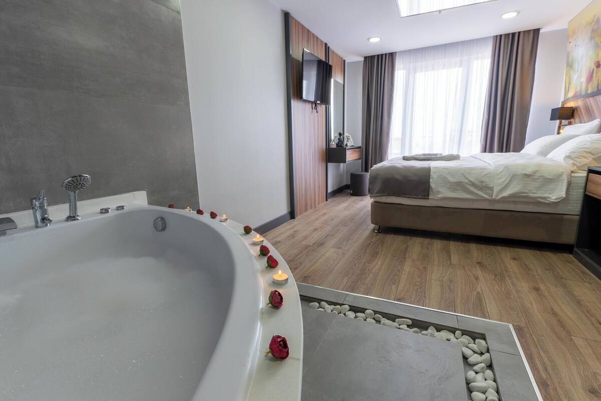 Ett modernt hotellrum med ett stort badkar, en säng och en tv som är monterad på väggen.