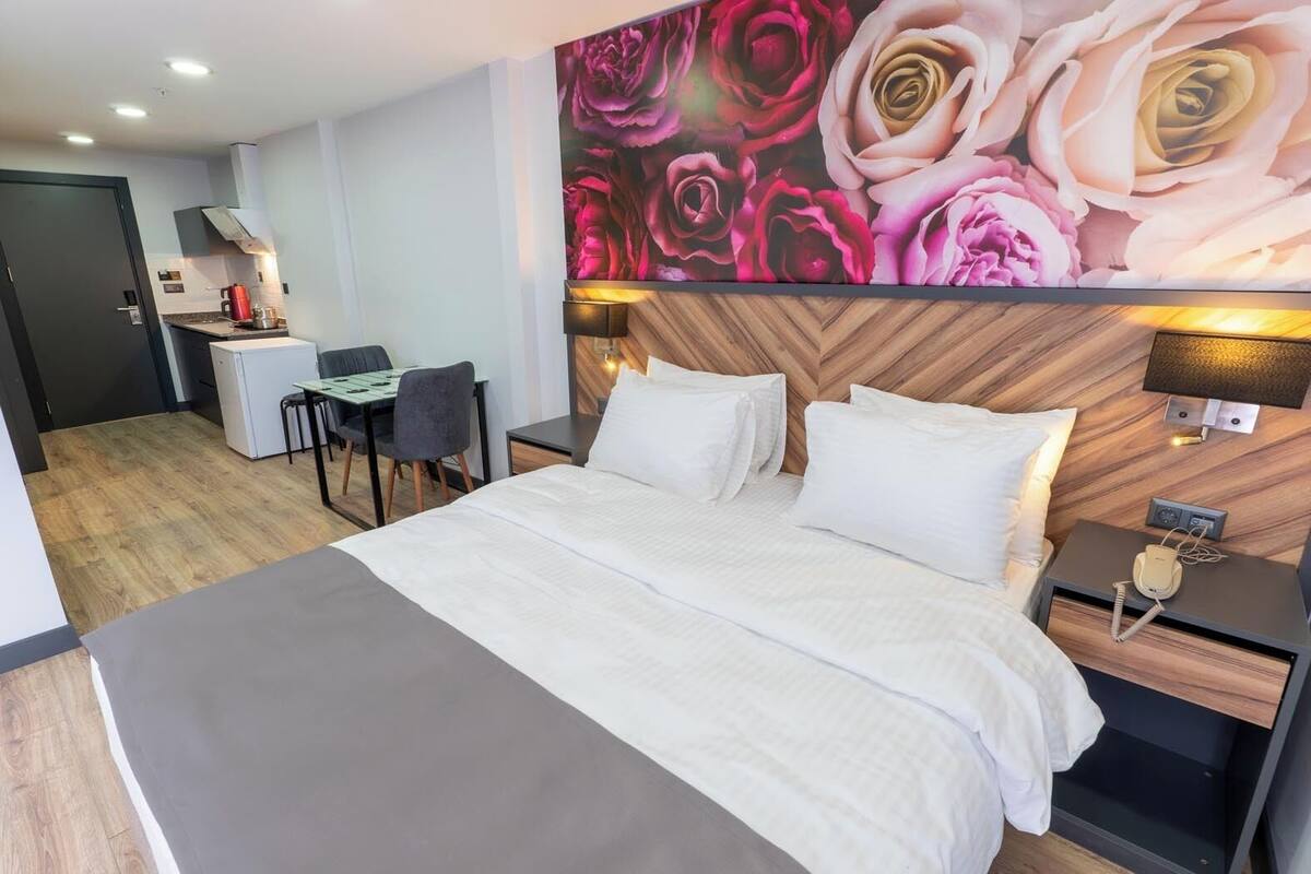 Ett hotellrum med en stor säng, ett skrivbord med en stol, ett litet pentry och en vägg prydd med en blommig väggmålning.