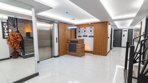 Un área de recepción moderna de hotel con un mostrador de recepción, una escalera y un reloj montado en la pared.