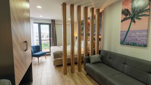 Una habitación de hotel moderna con un separador de madera, un sofá, una cama y un ventanal con vistas a la ciudad.