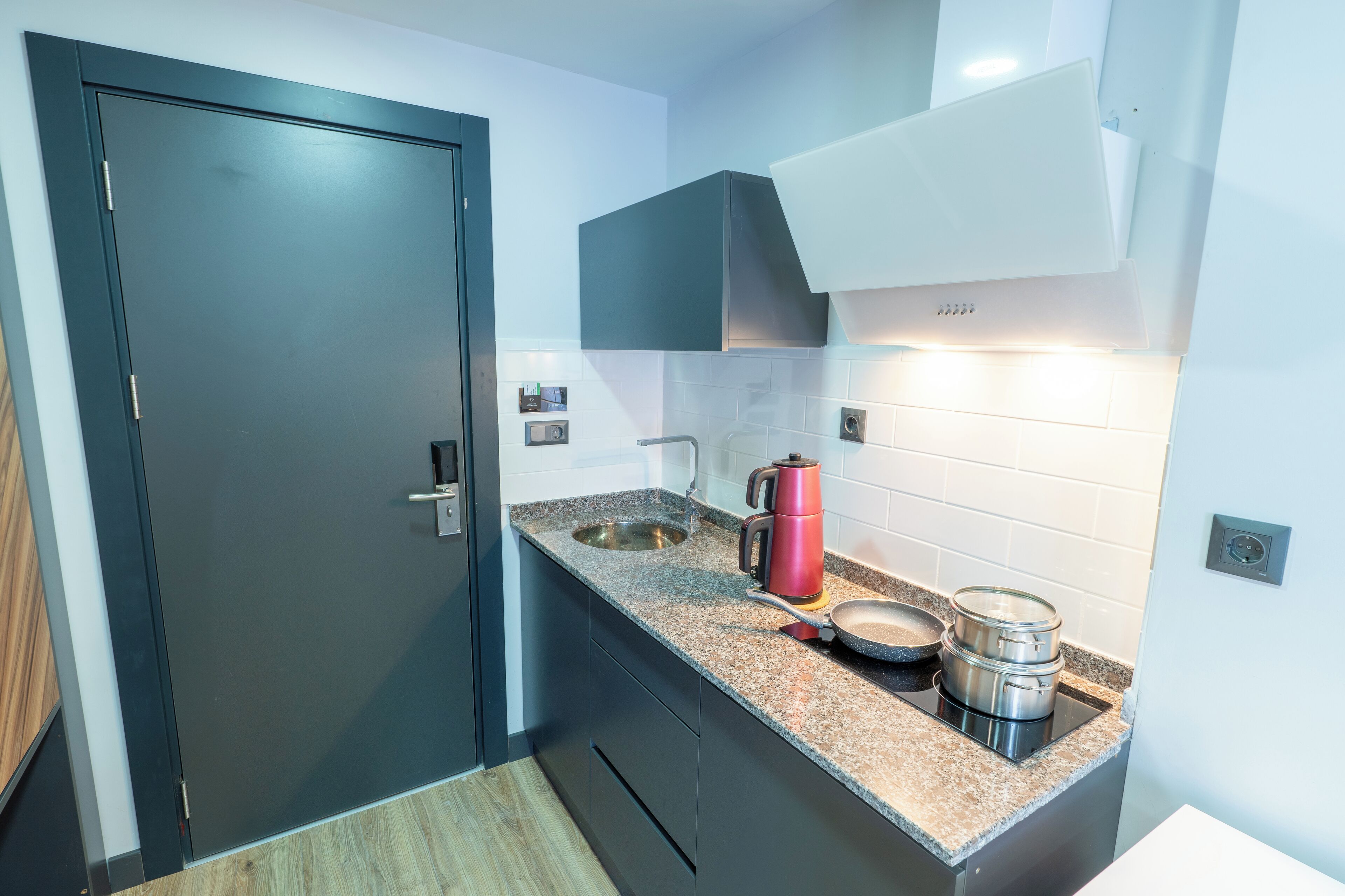 A compact kitchen with a dark door, white tiled backsplash, and stainless steel appliances.