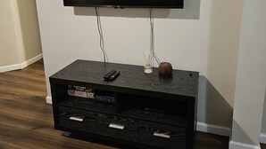 Ein Flachbildfernseher an einer dunklen Holz-Unterhaltungseinrichtung, mit Fernbedienung und dekorativen Gegenständen darauf.