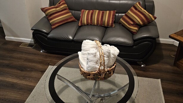 Ein Wohnzimmer mit einem schwarzen Ledersofa, gestreiften Kissen, einem gewebten Korb mit Handtüchern und einem Glastisch auf einem Streifenmuster-Teppich.