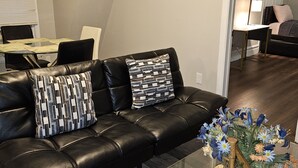 A modern living room with a black leather sofa, a glass coffee table, and a floral centerpiece.