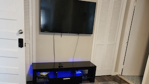 A room with a flat-screen TV mounted on the wall, a glass-top coffee table, and a dark wooden floor.
