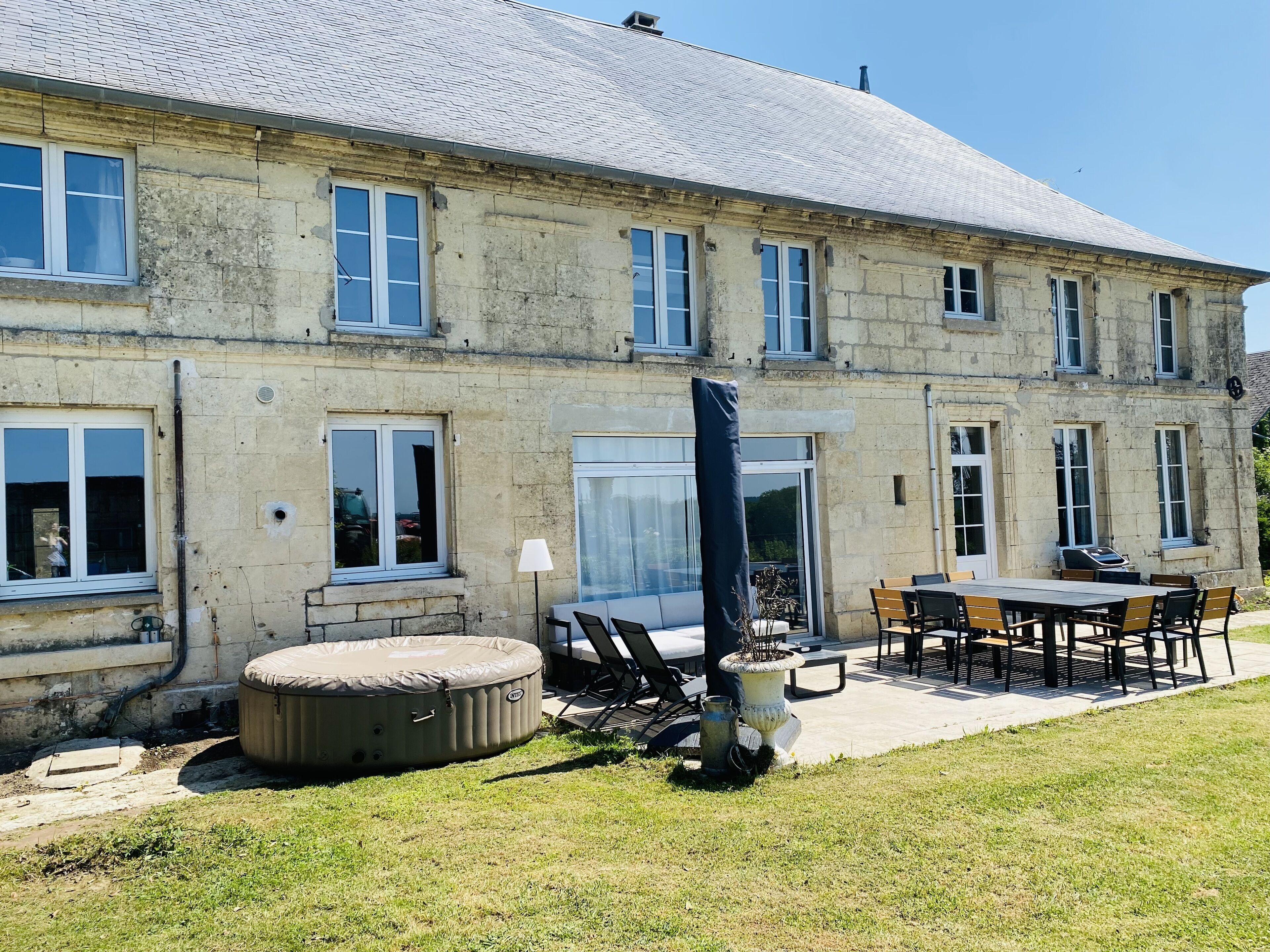 Ein großes Steinhaus mit vielen Fenstern und einer überdachten Terrasse mit Gartenmöbeln.