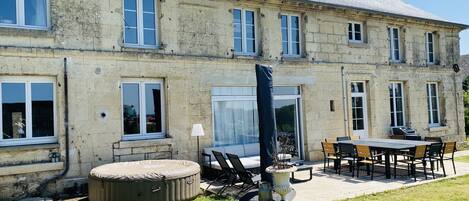Ein großes Steinhaus mit vielen Fenstern und einer überdachten Terrasse mit Gartenmöbeln.