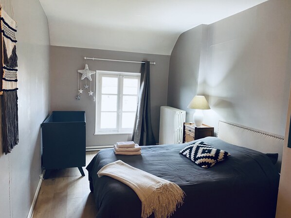 Un dormitorio con cama, mesita de noche, lámpara, radiador, ventana con cortinas y decoración con estrellas.