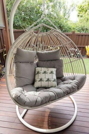 Relax in a hanging chair with a cushioned seat and backrest, surrounded by lush greenery and a wooden deck.