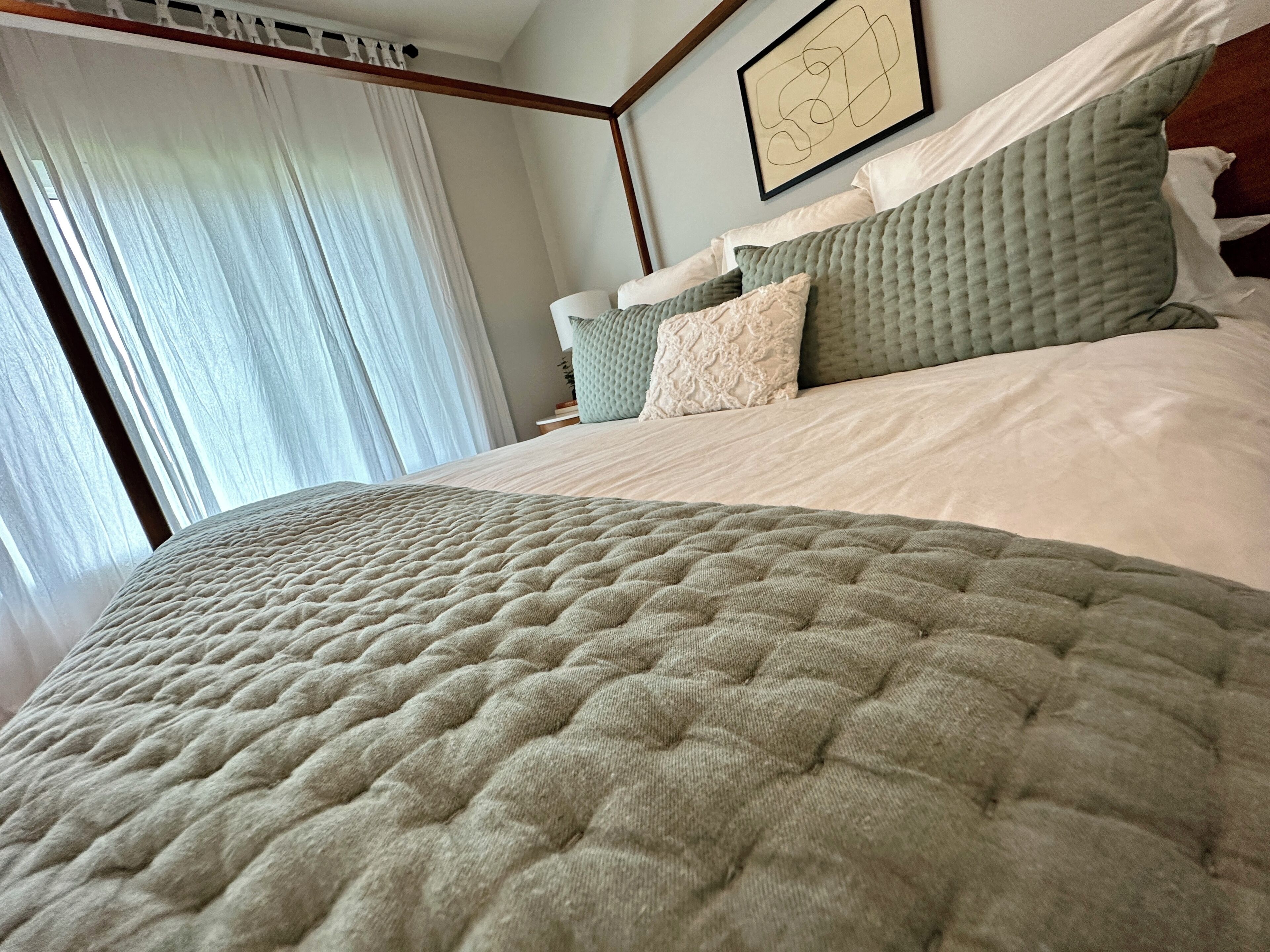 Una cama bien hecha con un edredón acolchado, un cabecero con almohadas y un cuadro en la pared.