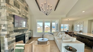 A spacious living room with a stone fireplace, a large sofa, a coffee table, and a dining area with a bar.