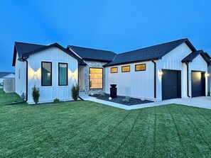 A modern two-story house with a well-maintained lawn, a stone facade, and a garage with a black door. - Modern Farmhouse - 4 Bd 3 Bth (Lincoln)