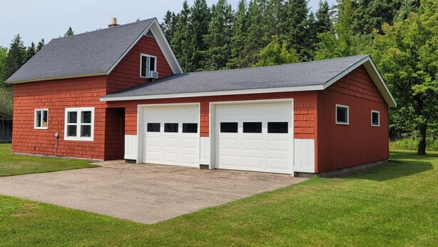 A red single-story house with two attached garages and a paved driveway. - The Red House -  modern beautiful Scandinavian style cozy cottage! (Chassell)