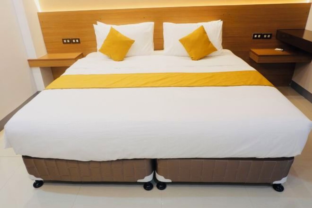 Una cama doble con cabecera de madera, dos mesitas de noche y un corredor amarillo decorativo.