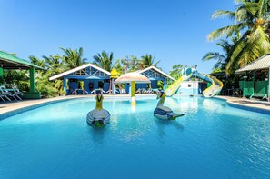 A swimming pool with two swan-shaped floats, palm trees, and a water slide.