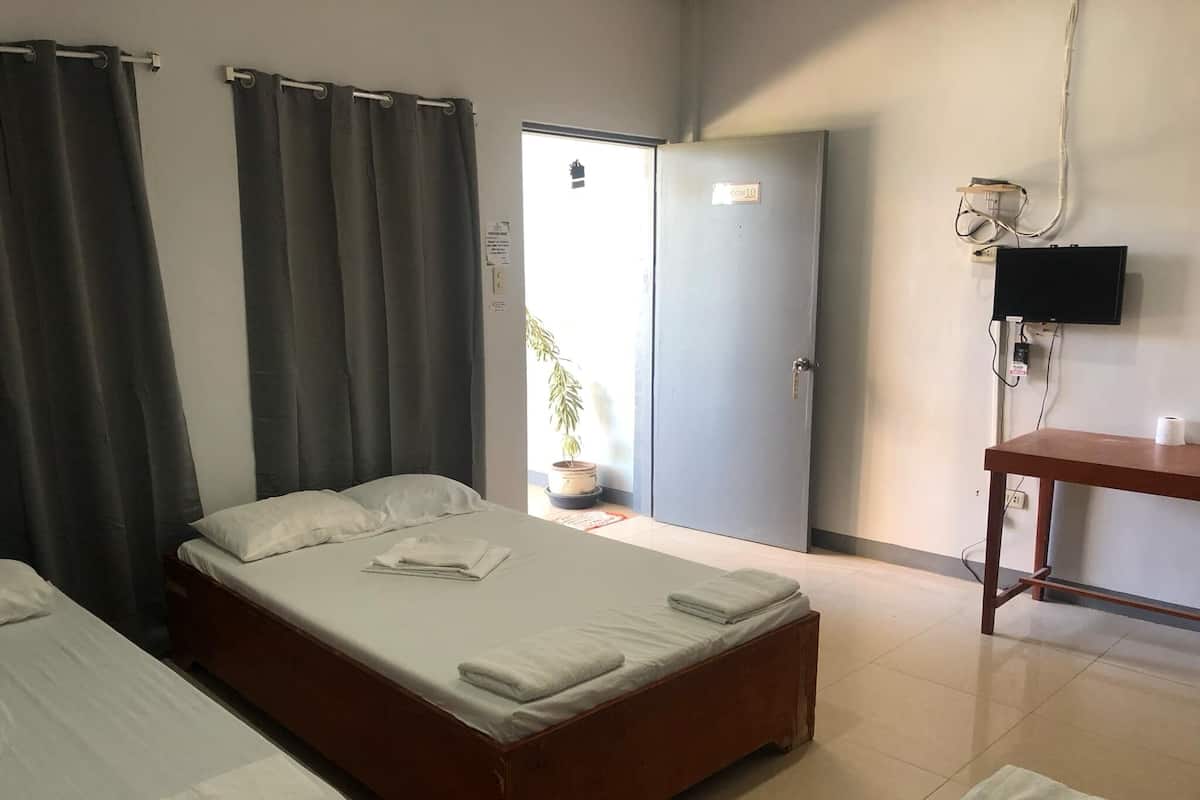A hotel room with two beds, a desk, a television, and a door leading to a balcony.