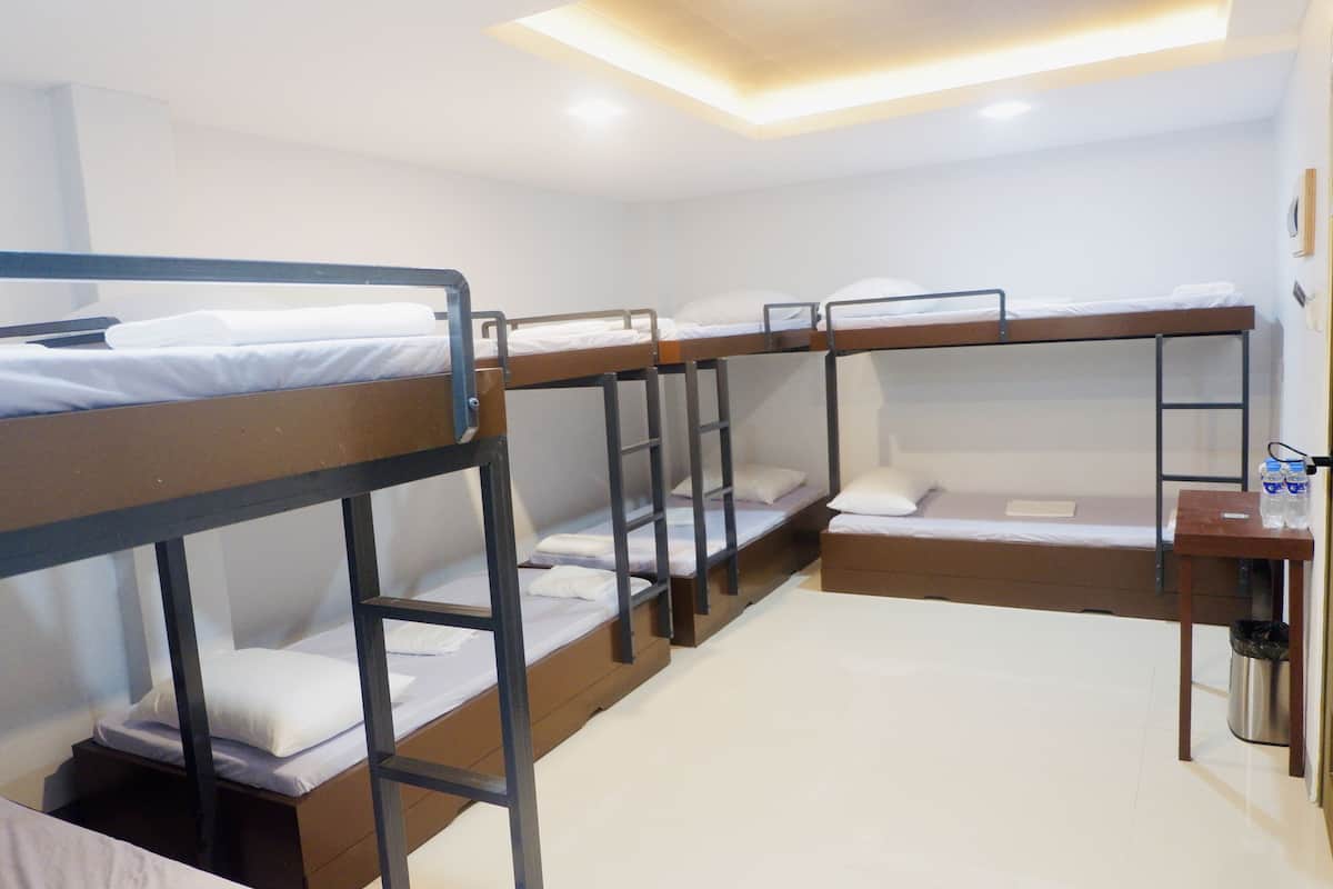 A dormitory room with bunk beds, a small desk, and a trash bin.