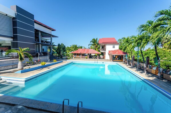 A swimming pool with a clear blue water, surrounded by palm trees and a building with a red roof.