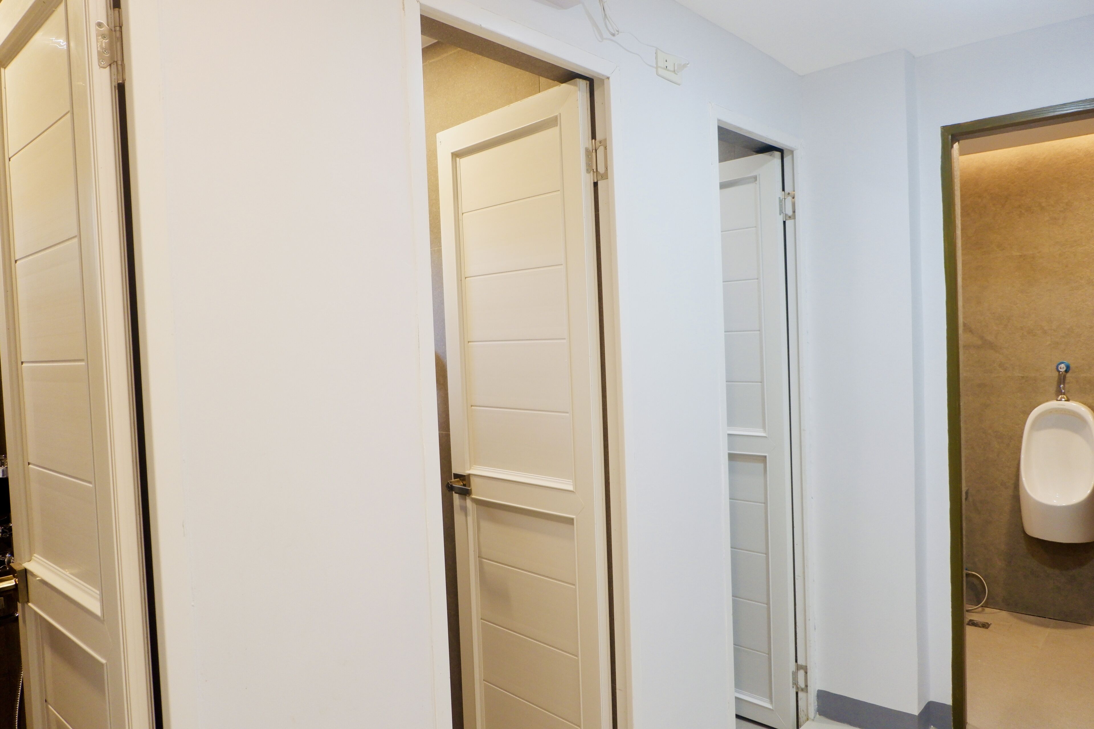 A hotel bathroom with white tiled walls, a urinal, and a door leading to another room.