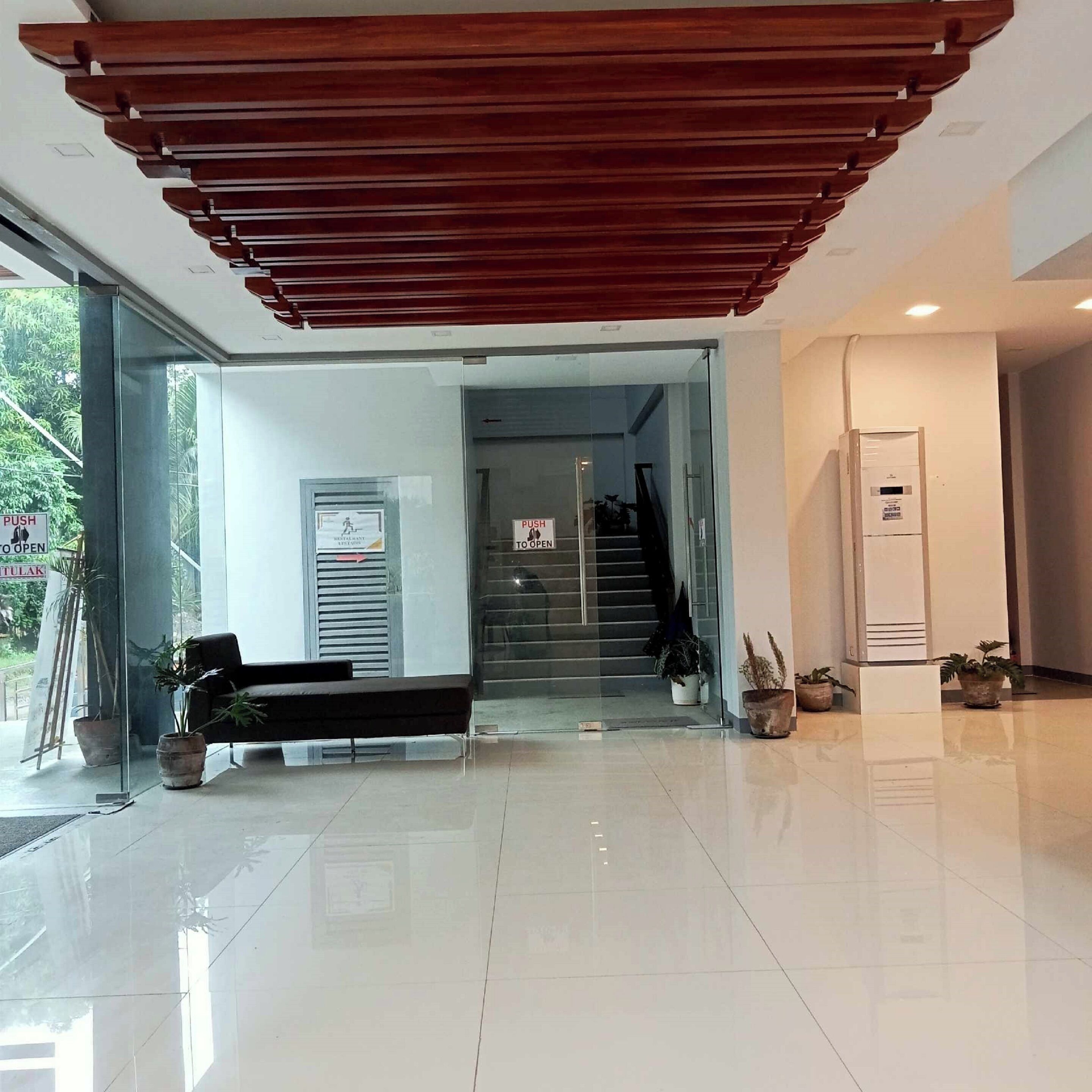 A modern lobby with a reception desk, a staircase, and potted plants.