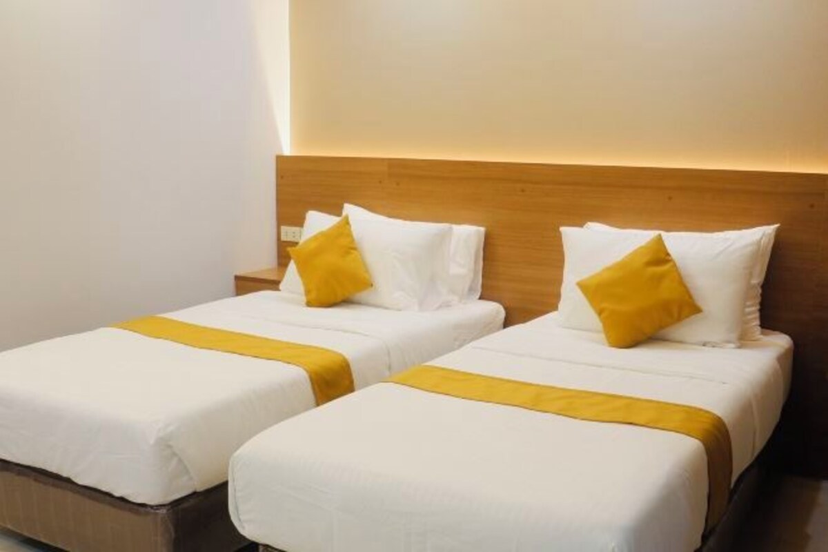 Habitación de hotel con dos camas individuales, cada una con colchón blanco y edredón amarillo.