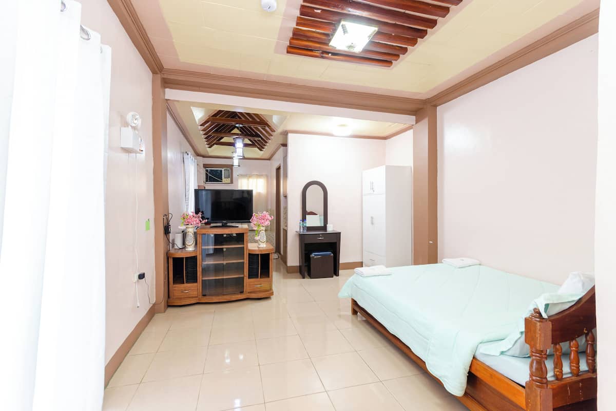 A bedroom with a bed, a TV, a mirror, and a small desk with a lamp.