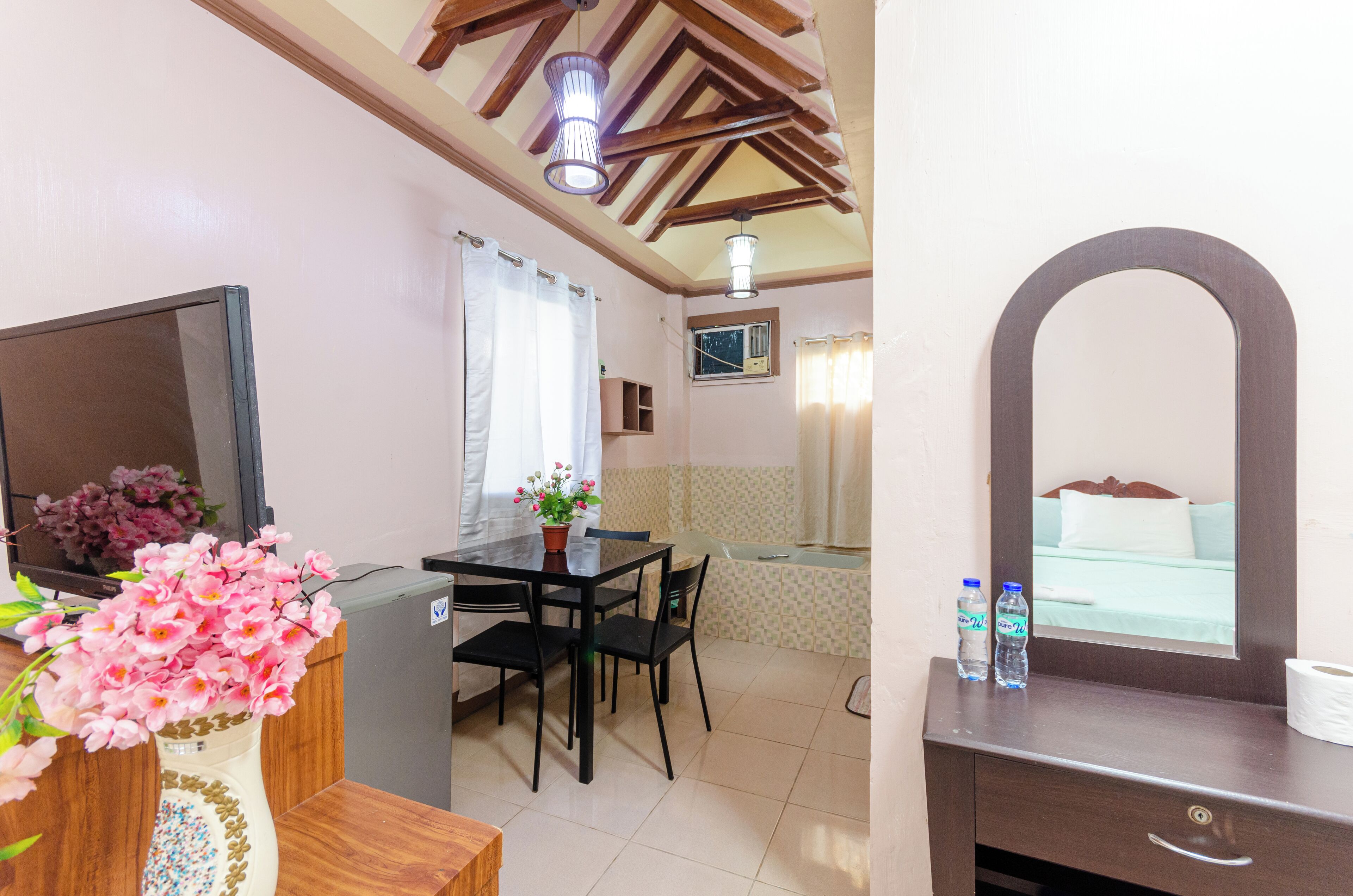 A hotel room with a dining area, a TV, a mirror, and a bed with a view.