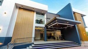 Entrada moderna d'un hotel amb una zona exterior coberta, escales cap a l'entrada i una porta de vidre.