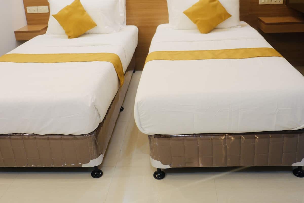 Two single beds with white bedding and yellow accents, wooden headboards, and bedside tables with lamps.