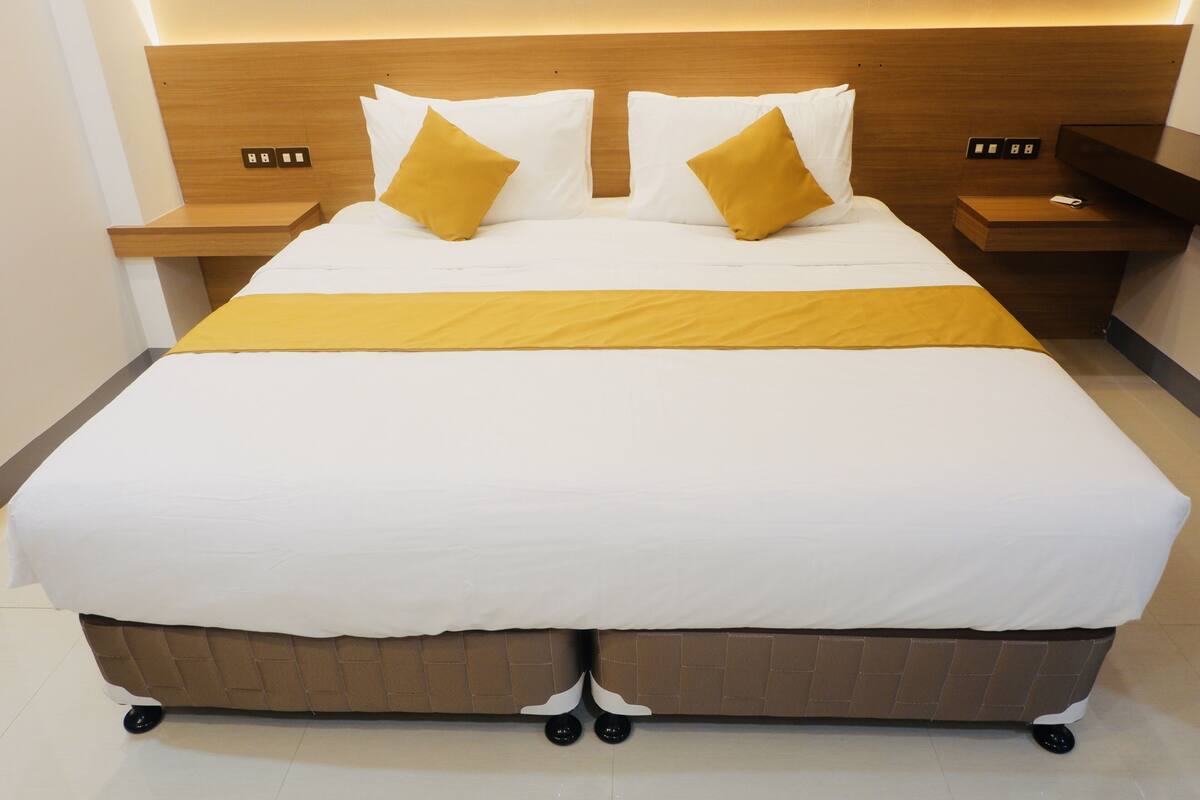 A large bed with a wooden headboard, two bedside tables, and a yellow accent pillow.