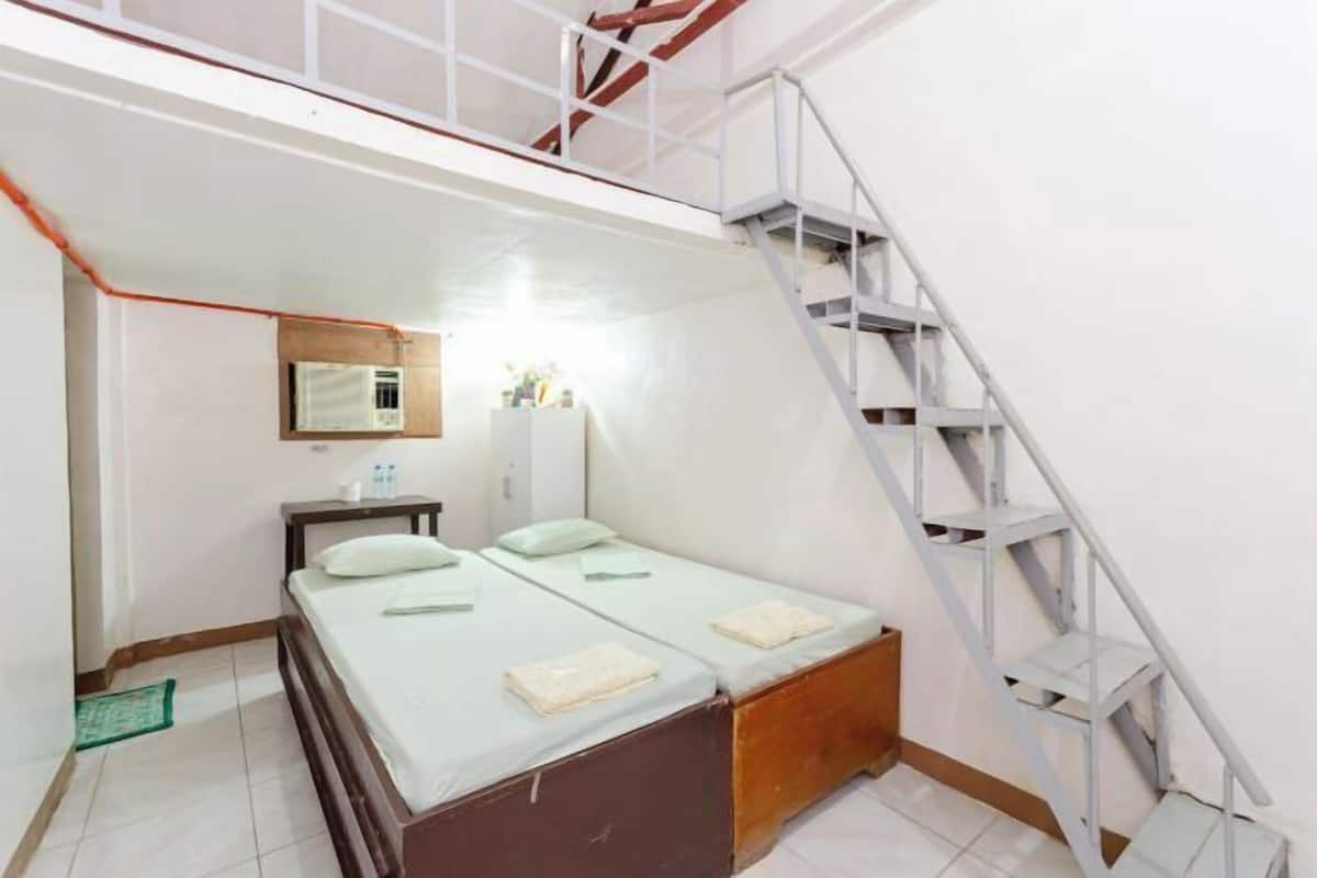 A small, compact room with a bed, a desk, a chair, a mirror, and a staircase.