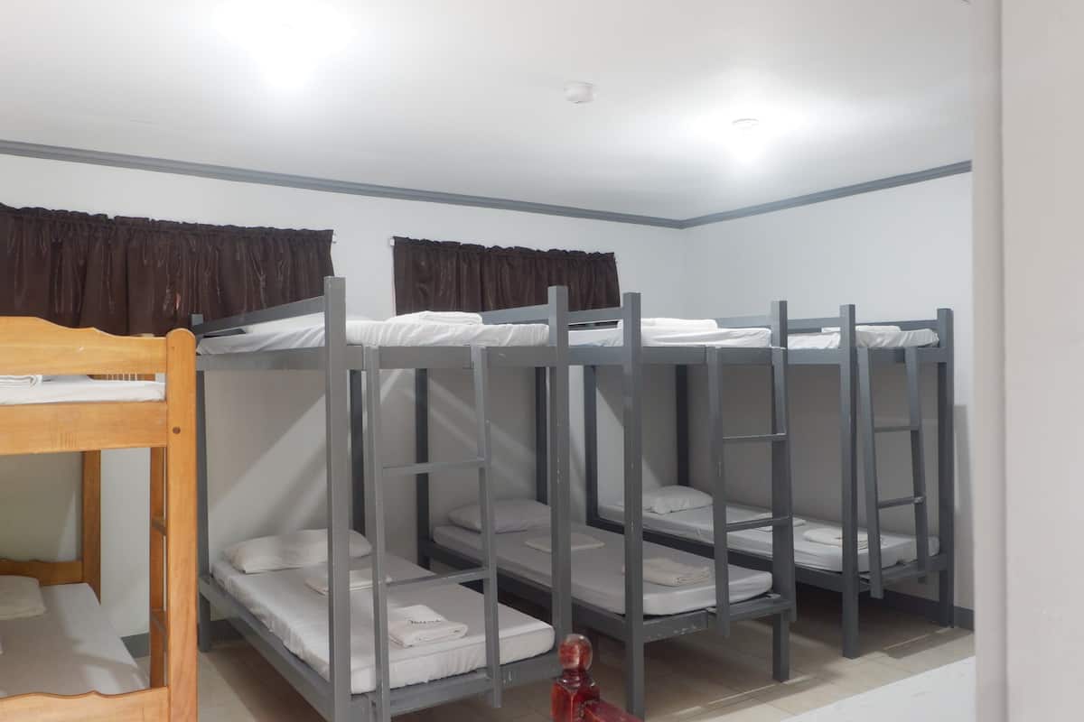 A dormitory room with bunk beds, a wooden bed at the corner, and a ceiling light.