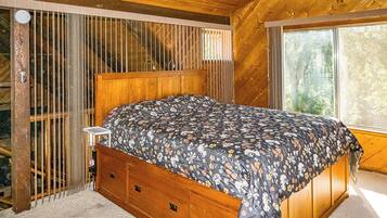 A wooden-framed bed with a floral bedspread in a room with a large window and a view of trees.