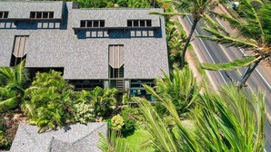 Un bâtiment moderne avec un toit en tuiles, entouré d’une végétation luxuriante et de palmiers.