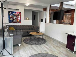 En moderne stue med en grå modulsofa, et rundt sofabord og et tv ophængt på en trævæg.