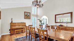 Ein Esszimmer mit einem hölzernen Klavier, einem Esstisch, Stühlen und einer Chandelier.
