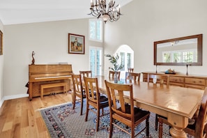 A dining area with a wooden table, chairs, a piano, and a chandelier.