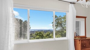 Ein Schlafzimmer mit großem Fenster, einem hölzernen Schminktisch und einem Bett mit gemustertem Überwurf.