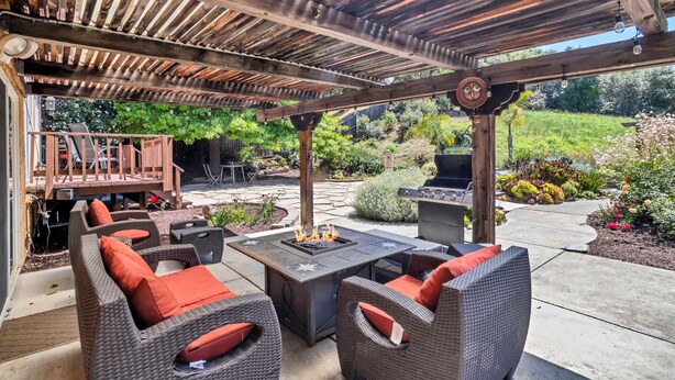 Eine überdachte Terrasse mit Gartenmöbeln, einem Feuerkorb und einem Grill.